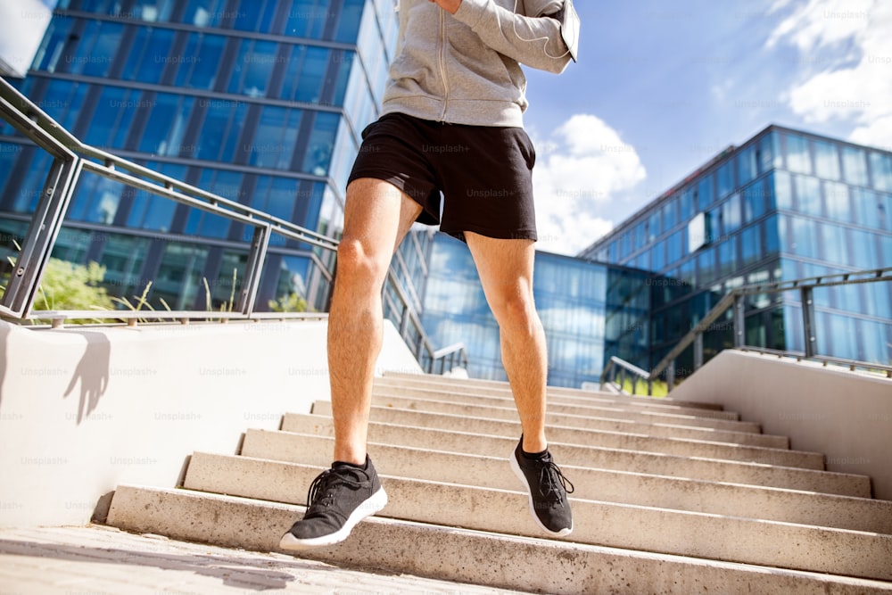 Atleta irreconhecível na cidade correndo em escadas em frente a prédios de vidro.