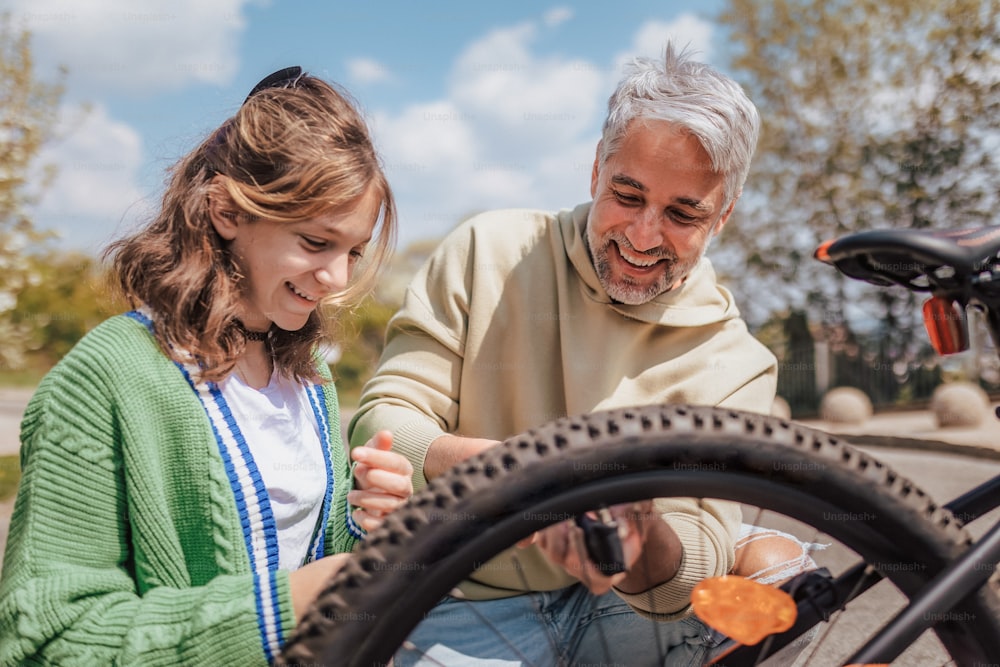 마을의 거리에서 자전거를 수리하는 십대 딸과 함께 행복한 아버지.
