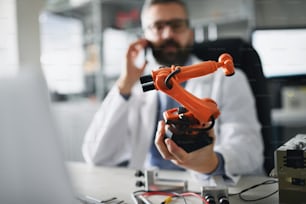 実験室でラップトップで作業するロボット工学エンジニアの手に持ったロボットアームの産業用ミニチュアフィギュア。