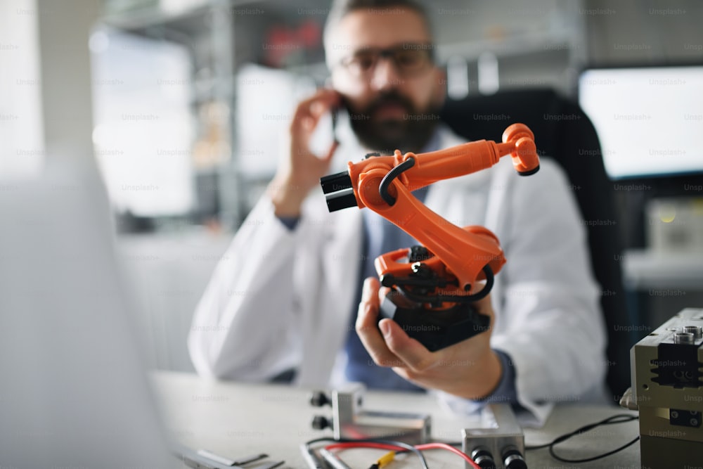 Uma figura em miniatura industrial de braço robótico na mão do engenheiro de robótica que trabalha em laptop em laboratório.