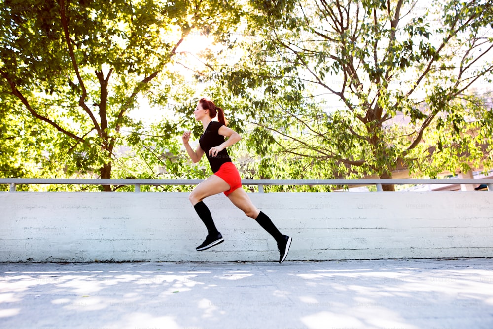 Belle jeune athlète en tenue de sport en train de courir sur un chemin en béton dans la ville.