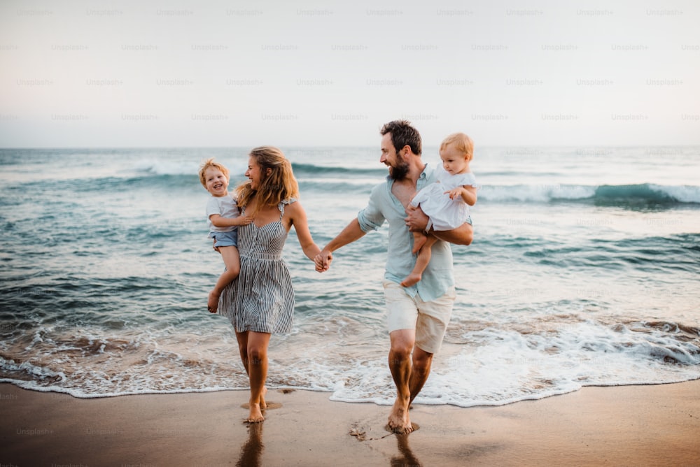 Eine junge Familie mit zwei Kleinkindern, die im Sommerurlaub am Strand spazieren gehen.