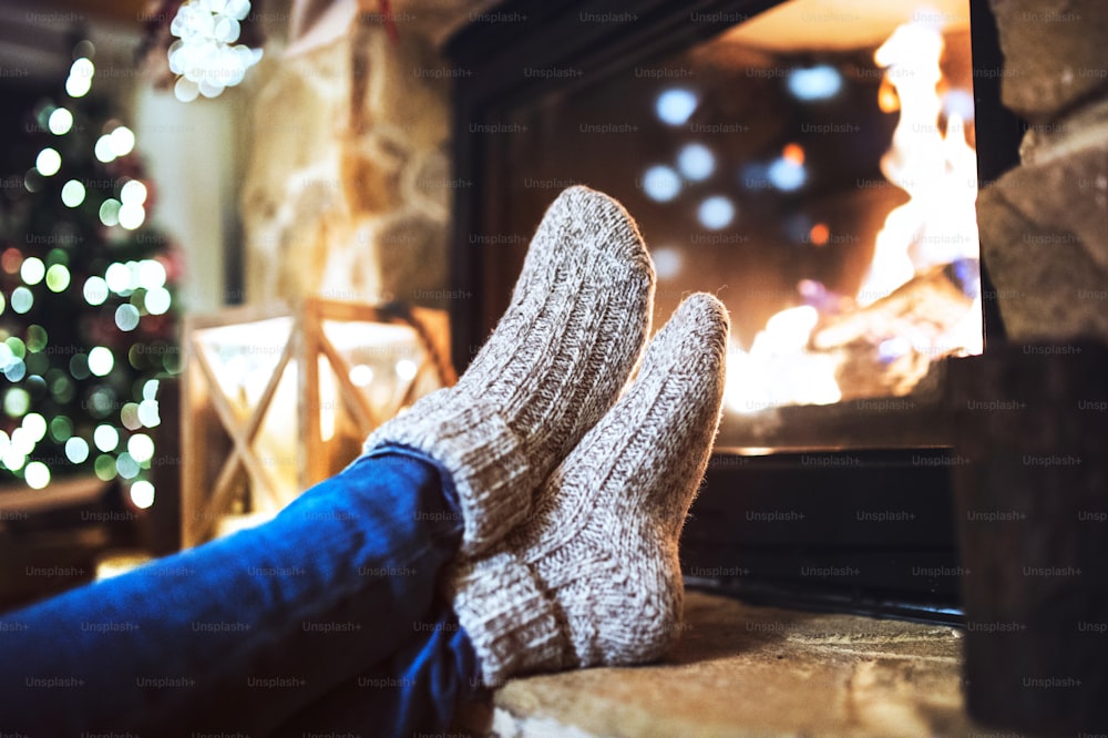 暖炉の前に座って休んでいる見分けのつかない女性の足。クリスマスの時期。