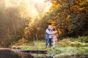 Casal idoso ativo em uma caminhada em uma bela natureza de outono. Uma mulher e um homem à beira do lago no início da manhã, se beijando.