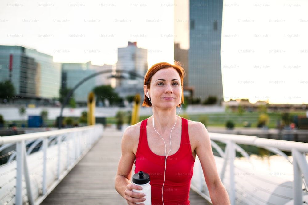 Young woman runner with water bottle in city, resting on the bridge. Copy space.