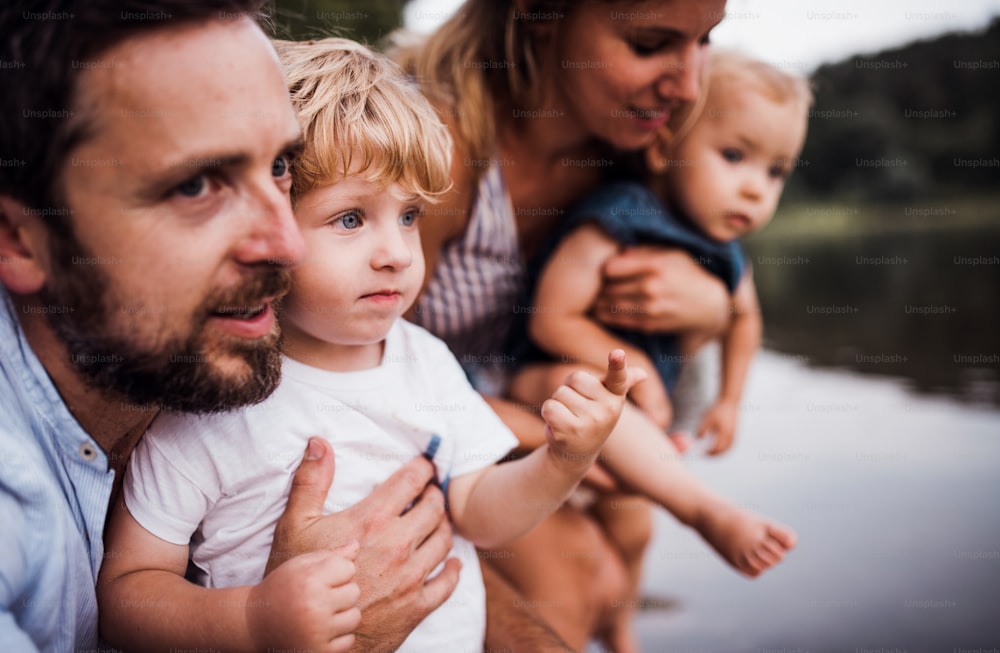 Eine junge Familie mit zwei Kleinkindern, die im Sommer Zeit im Freien am Fluss verbringen, eine Nahaufnahme.