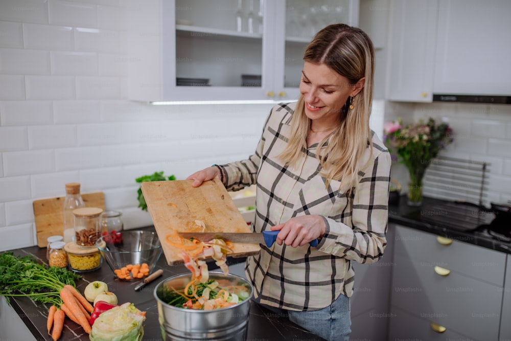 Una mujer arrojando esquejes de verduras en un cubo de abono en la cocina.