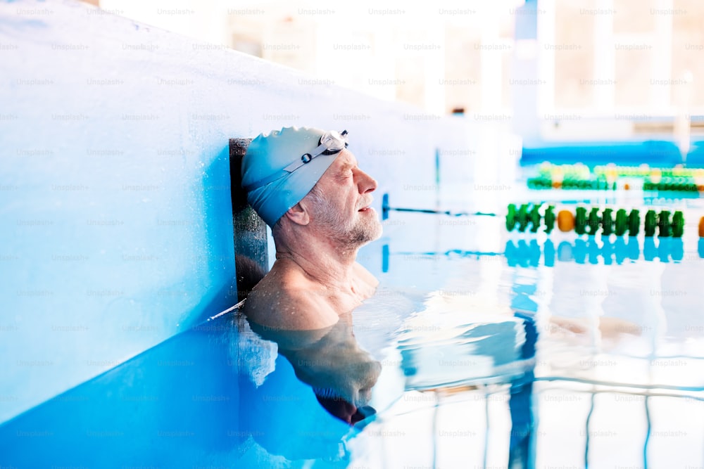 Homme âgé nageant debout dans l’eau dans une piscine intérieure. Retraité actif qui fait du sport.