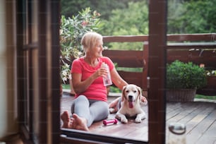 A senior woman with dog outdoors on a terrace in summer, resting after exercise.