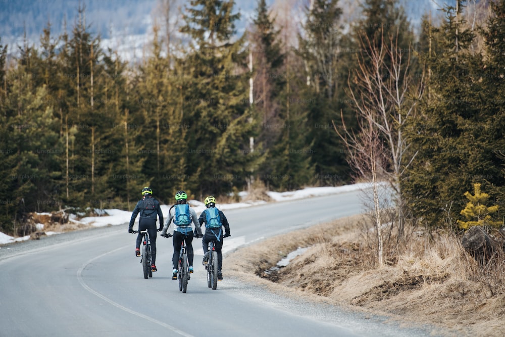 Rear view of group of mountain bikers riding on road in mountains outdoors in winter.