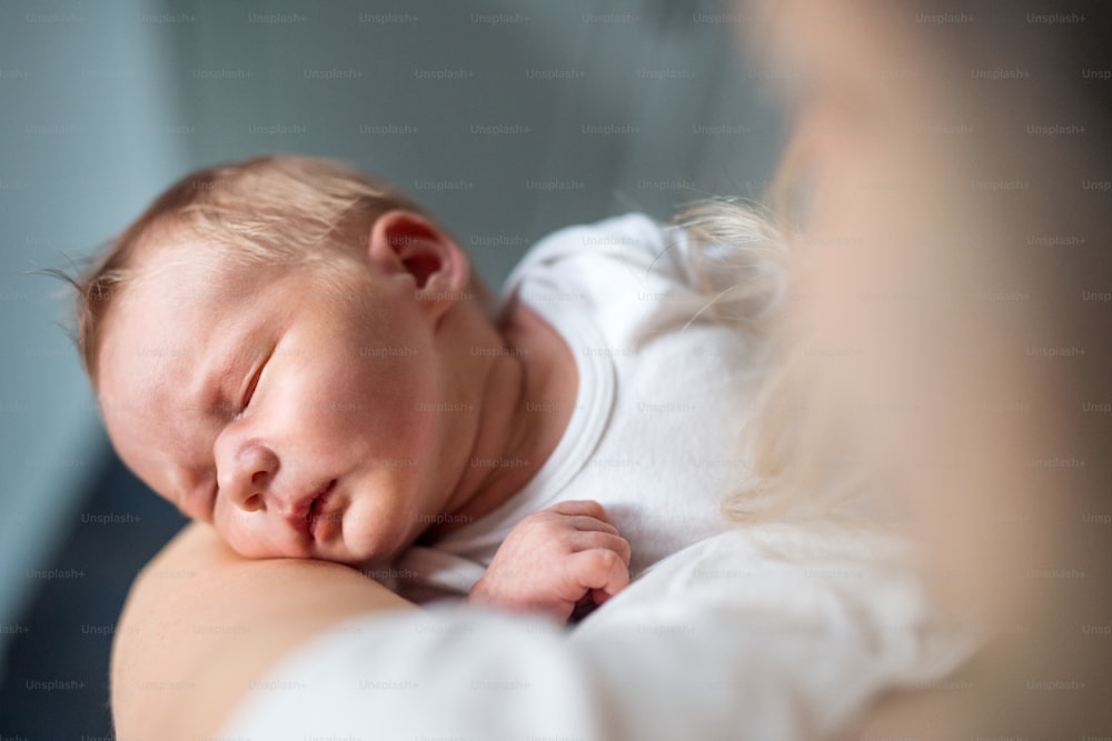 Un primo piano di una madre irriconoscibile che tiene in braccio un neonato addormentato a casa.