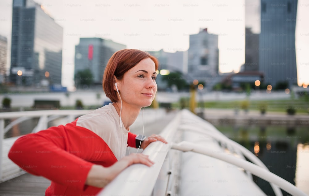 Vista lateral de una joven corredora con auriculares en la ciudad, estirándose en el puente.