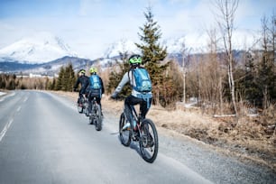 A rear view of group of mountain bikers riding on road outdoors in winter.