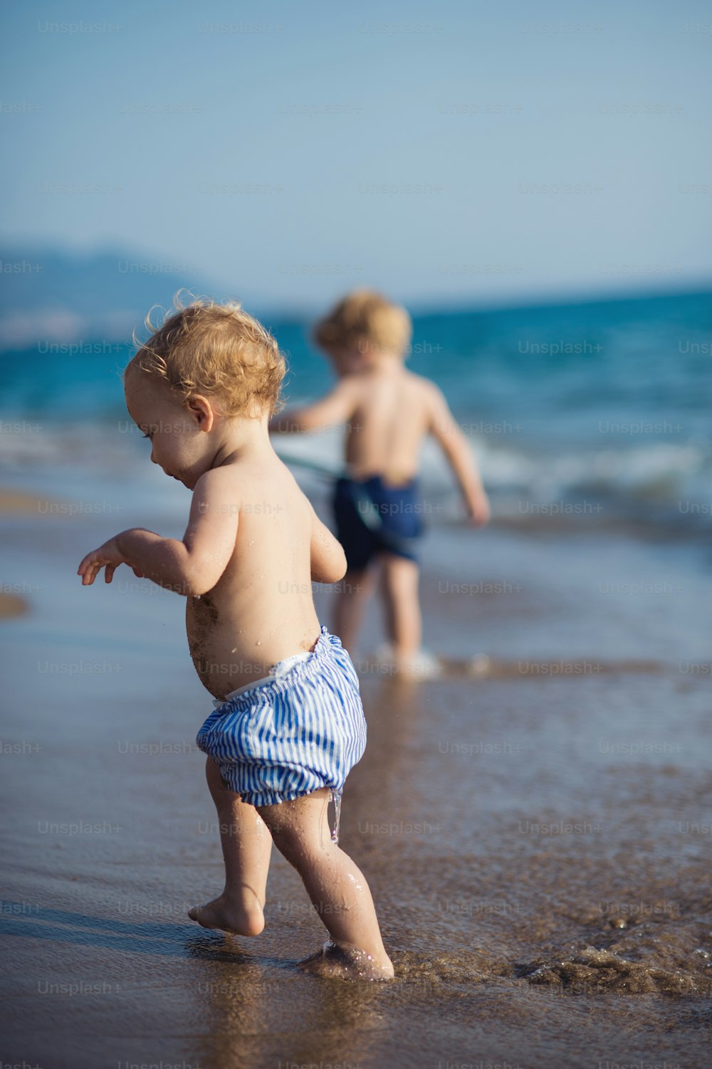 여름 휴가에 해변에서 걷고 있는 셔츠를 입지 않은 두 명의 유아.