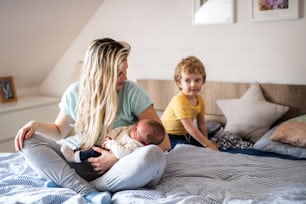 A beautiful young mother with a newborn baby and his toddler brother at home, sitting on bed.