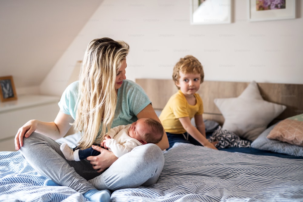 Una hermosa madre joven con un bebé recién nacido y su hermano pequeño en casa, sentados en la cama.
