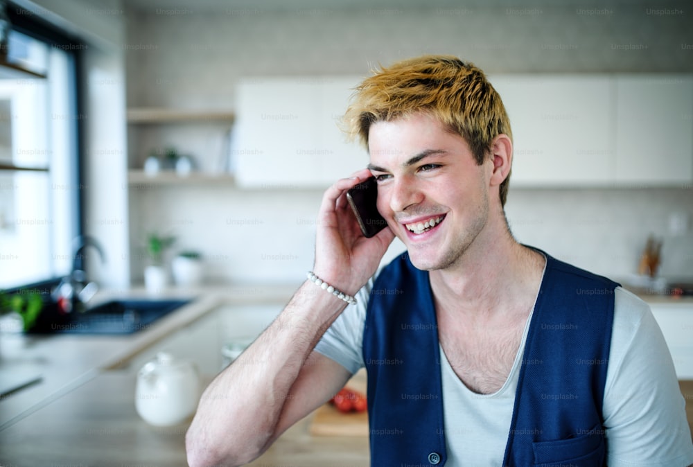 Un joven feliz con un teléfono inteligente en el interior de su casa, haciendo una llamada telefónica.
