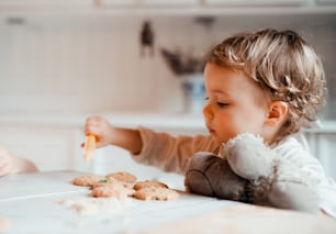 A happy small toddler girl sitting at the table, decorating cakes at home.