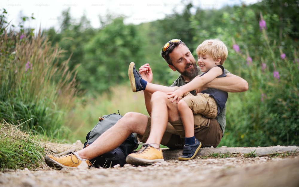 Mature father with small son hiking outdoors in summer nature, sitting and resting.
