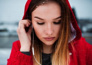 A close-up portrait of beautiful young girl or woman with earphones outdoors, listening to music.