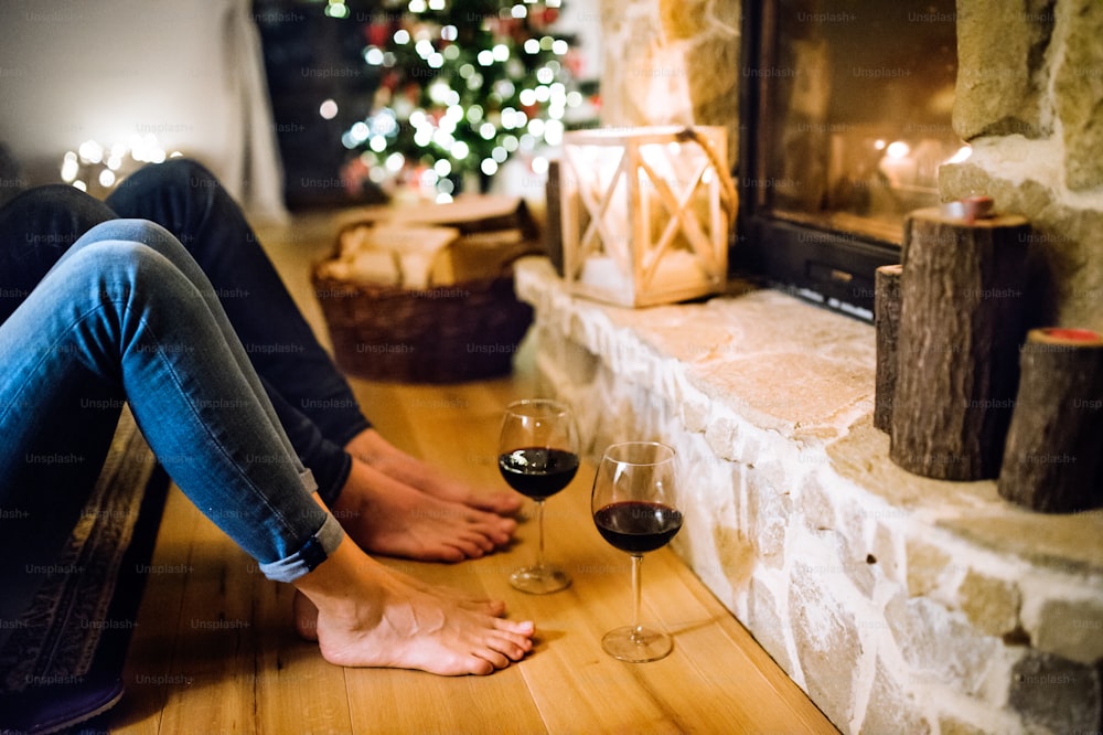 Jambes d’une femme et d’un homme méconnaissables assis devant la cheminée, se reposant. C’est la période de Noël.