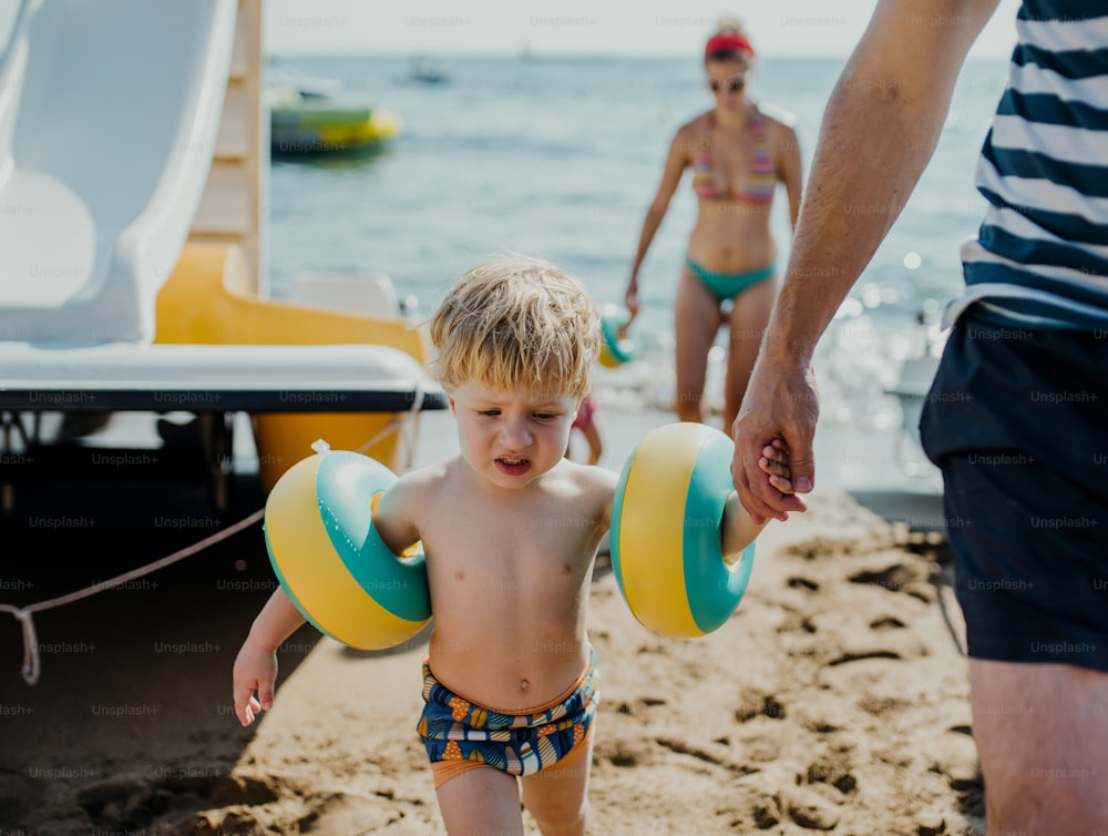 여름 휴가에 해변을 걷고 있는 두 명의 작은 유아 자녀가 있는 가족.