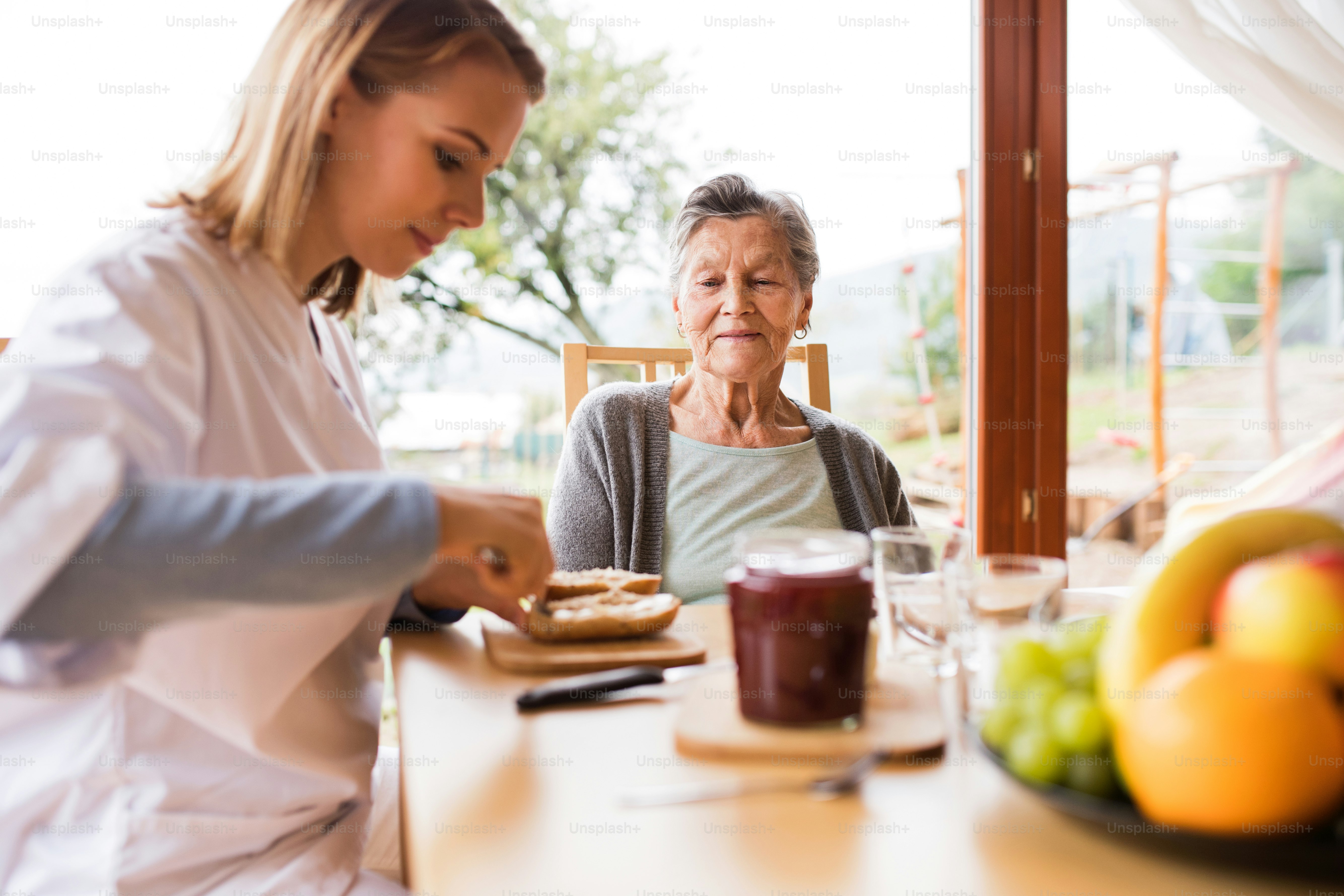 Visiteur de santé et une femme âgée lors d’une visite à domicile. Une infirmière et une femme âgée assises à table, préparant le petit-déjeuner.