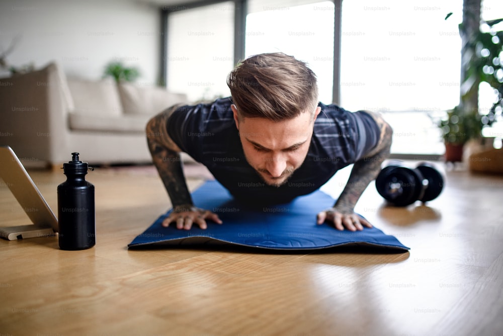 Front view portrait of young man with tablet doing workout exercise indoors at home.