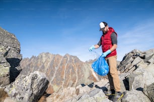 Mature man hiker picking up litter in nature in mountains, plogging concept.