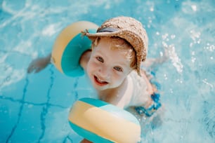 A happy small toddler boy with armbands swimming in water on summer holiday.