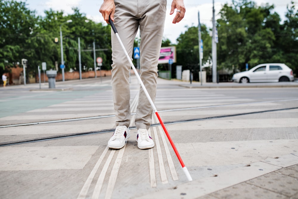 Abdomen d’un jeune homme aveugle méconnaissable avec une canne blanche marchant dans la rue en ville.