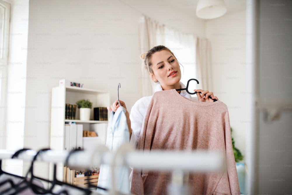 A young woman indoors at home in the morning, choosing clothes to wear.