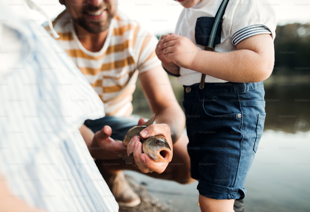 Un padre maturo con bambini piccoli che pescano da un fiume o da un lago, tenendo in mano un pesce.