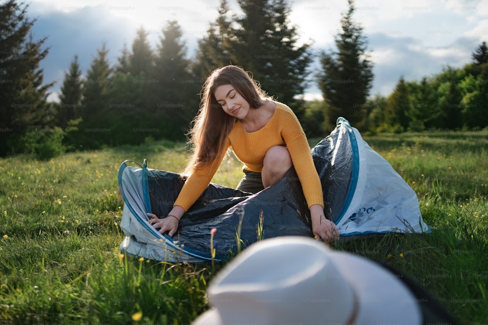 Front view of happy young woman using tent shelter outdoors in summer nature.