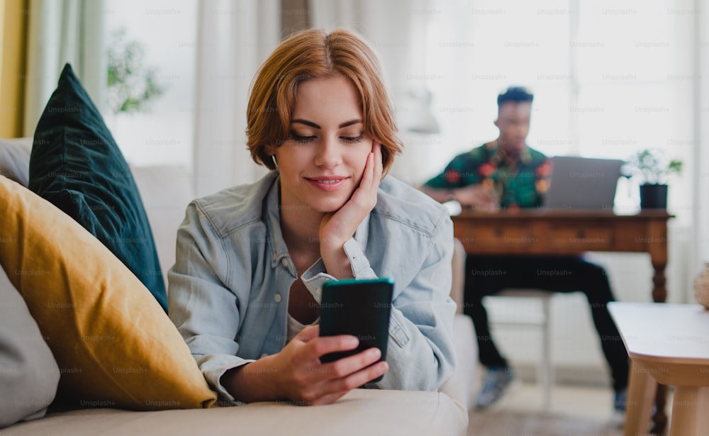 Happy young couple at home using digital divices, smartphone and laptop, socieal networks concept.Portrait of happy young woman using smartphone, lying on sofa at home, looking aside, social networks concept.