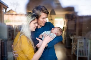 De beaux jeunes parents tenant un nouveau-né à la maison. Tiré à travers le verre.