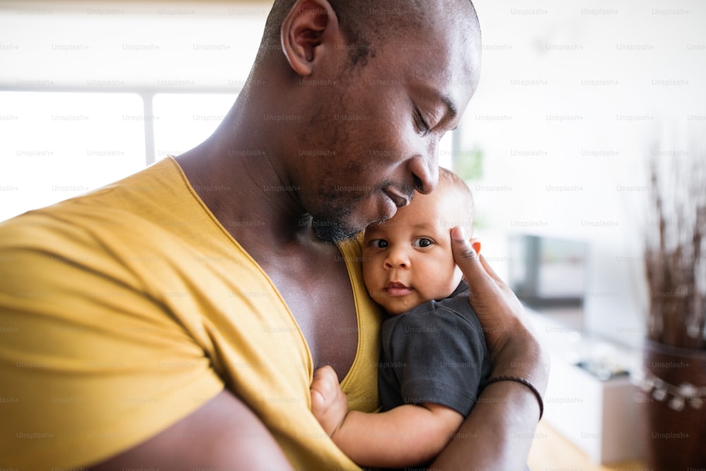 Jovem pai afro-americano em casa segurando seu filho bebê bonito em seus braços