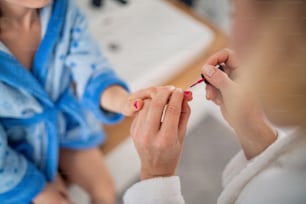 Midsection of mother painting nails of small daughter in bathroom indoors at home.