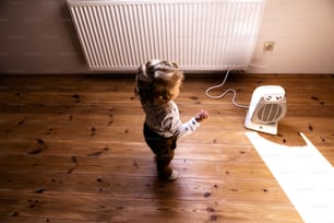 Cute little boy at home standing at the fan in bedroom.