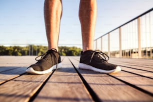 木製の橋の上に立つ黒いスポーツシューズを履いた見分けがつかないランナーの脚。
