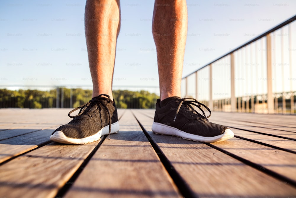 Jambes d’un coureur méconnaissable en chaussures de sport noires debout sur un pont en bois.