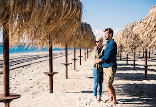 Young couple standing outdoors among straw umbrellas on beach, hugging. Copy space.