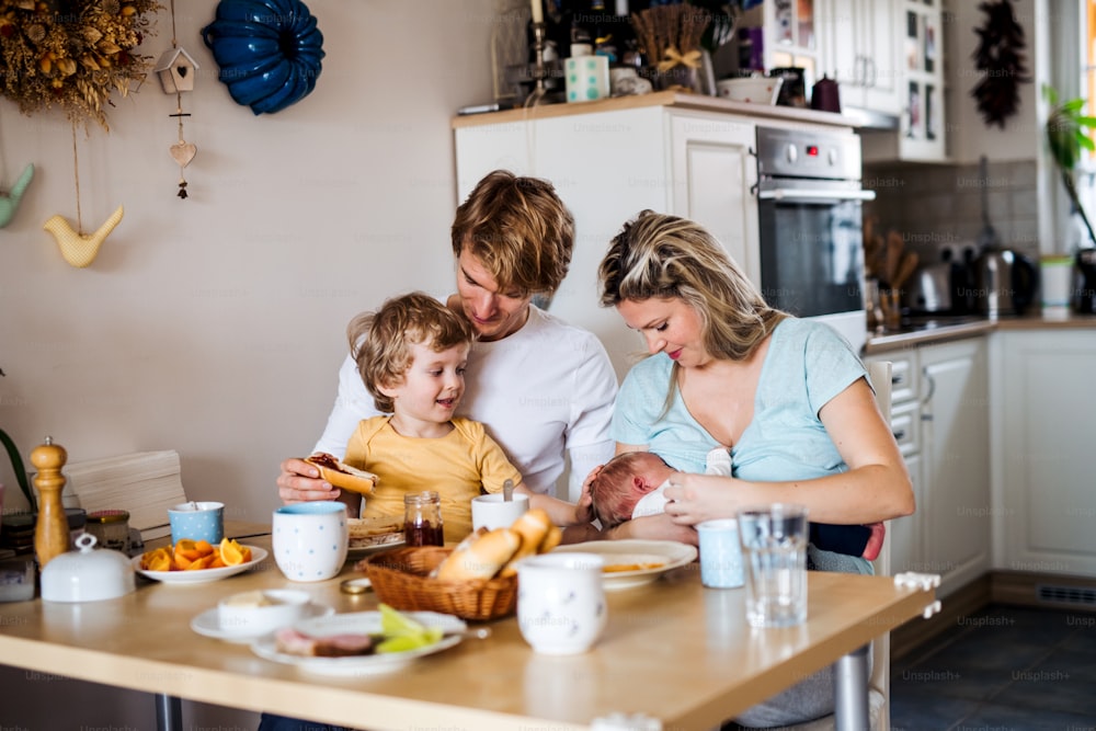 Giovani genitori con un neonato e un figlio piccolo seduti al tavolo di casa.