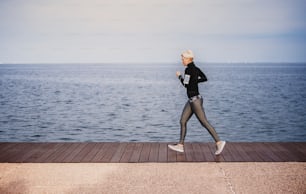 Side view of young sportswoman running outdoors on beach. Copy space.