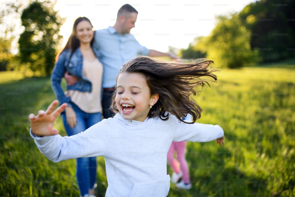 Familia feliz con dos hijas pequeñas divirtiéndose al aire libre en la naturaleza primaveral, corriendo.