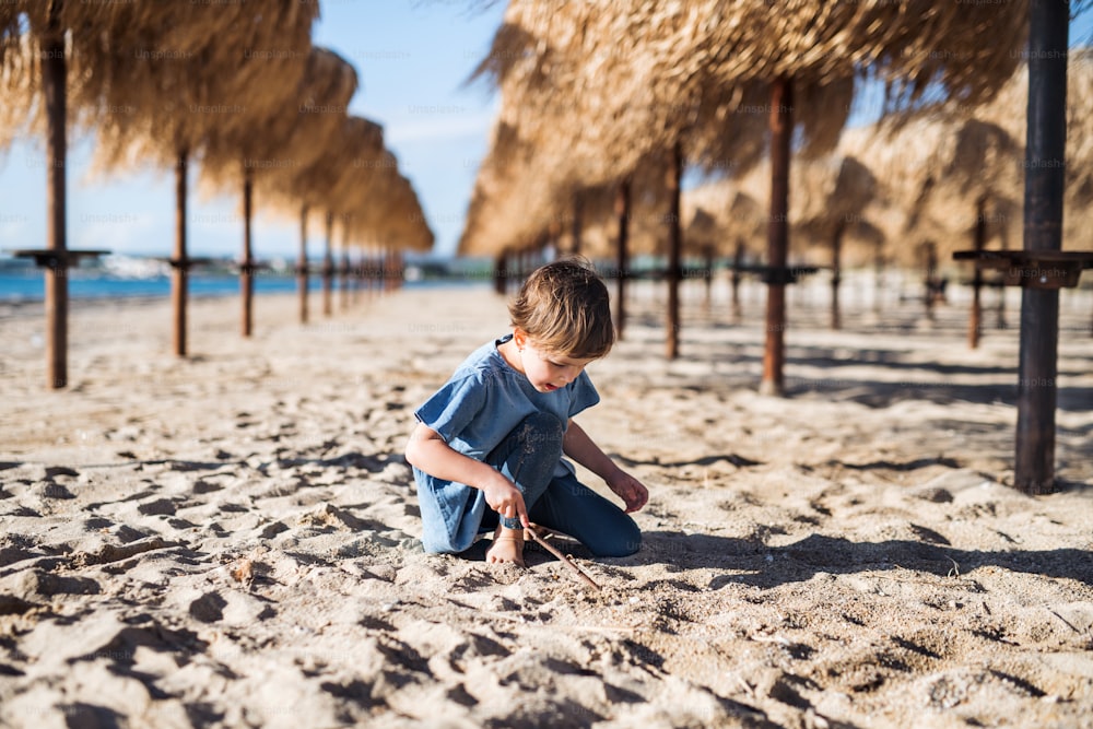 A small girl playing among straw parasols outdoors on sand beach.
