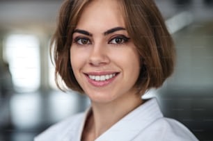 A young karate woman standing indoors in gym, looking at camera.