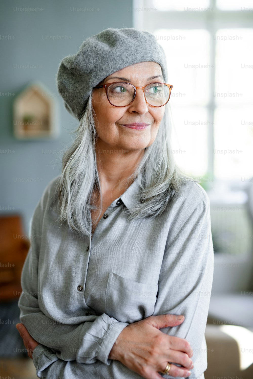 Studio portrait of senior woman with gray beret standing indoors against dark background.