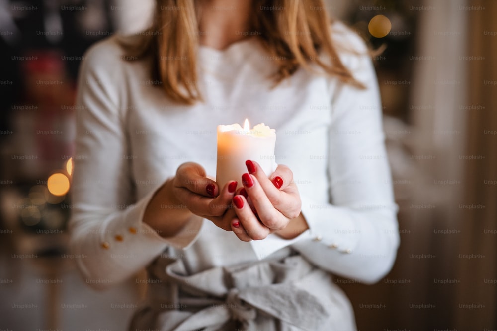 Joven adolescente irreconocible en el interior de su casa en Navidad, sosteniendo una vela.