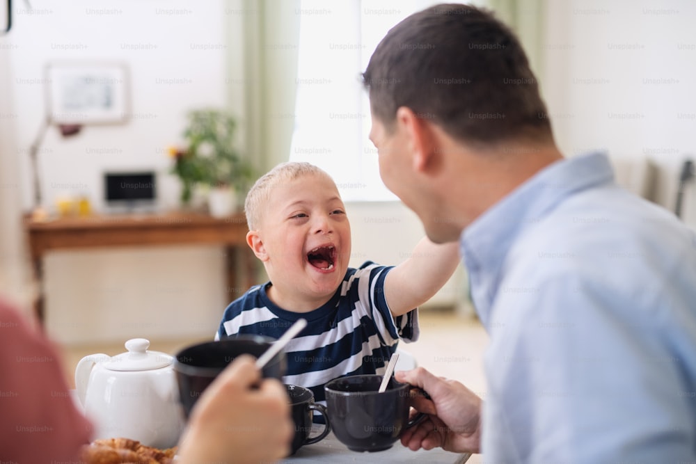 Une famille heureuse avec un fils trisomique à table, riant au petit-déjeuner.